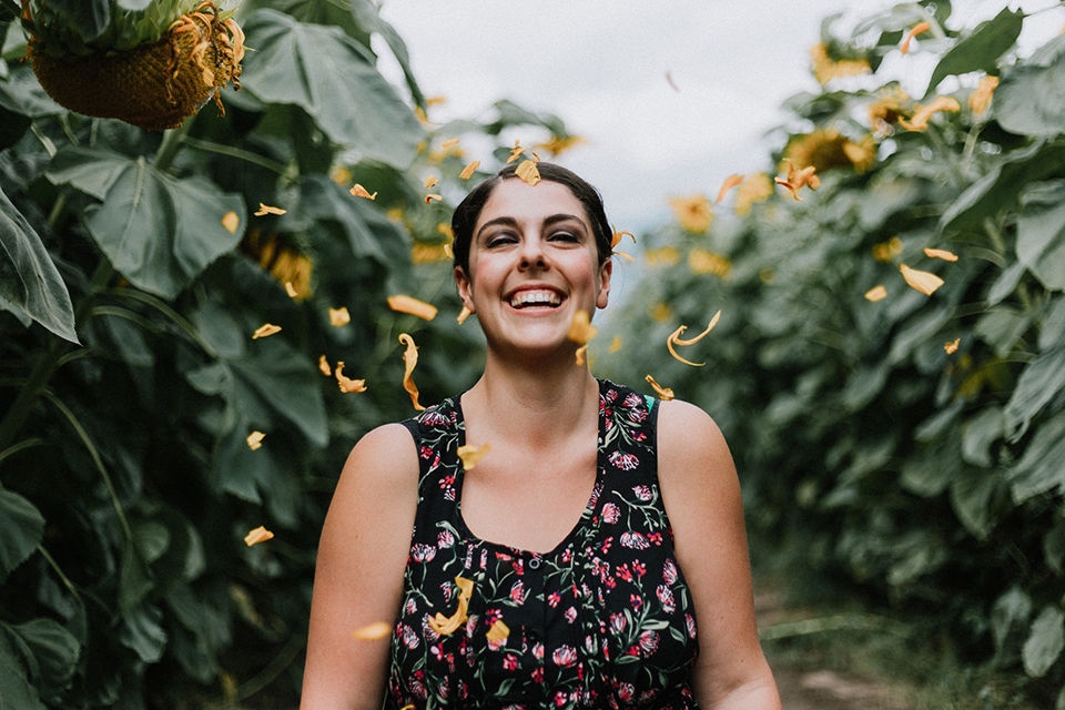 Smiling international student standing in a field with blossoms falling around her. 