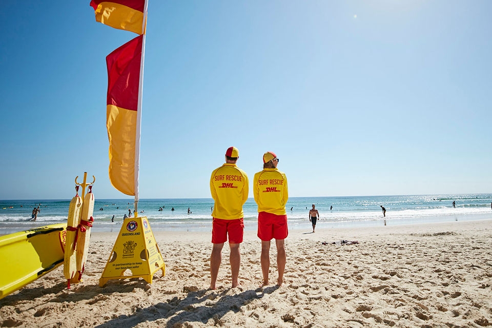 Two lifeguards stand on a beach watching swimmers in the ocean.  