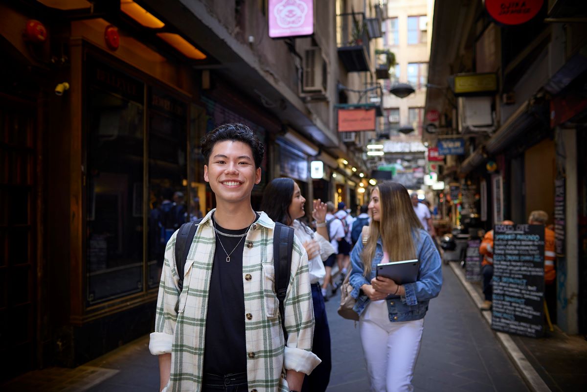 A young student smiling as he stands in a busy laneway in Melbourne