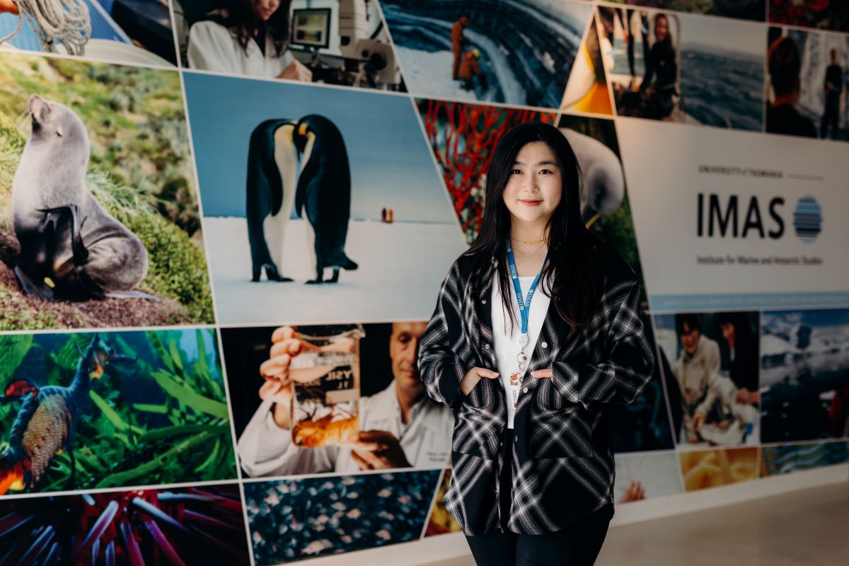 An international student standing in front of an IMAS branded wall 