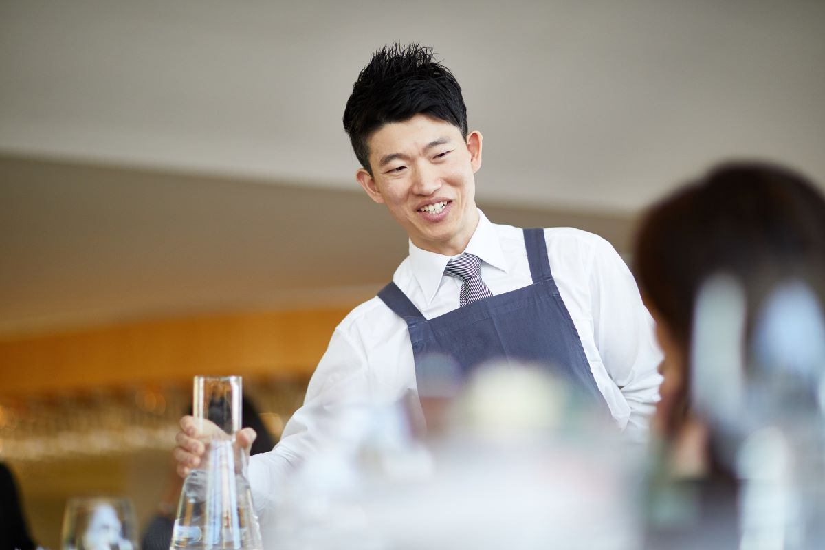 A waiter smiling while serving water to a customer